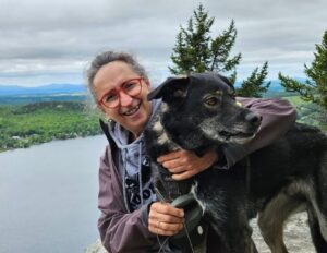 une femme souriante avec son chien noirau sommet d'un montagne